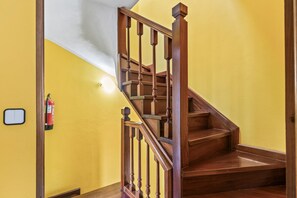 Una escalera de madera con barandilla, un extintor en la pared y un interruptor de luz.