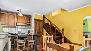 A kitchen with wooden cabinets, a dining table with chairs, and a staircase. - Casa Luis with Mountain Views (Llenín)