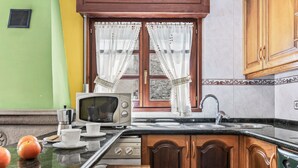 A kitchen with a microwave, sink, and wooden cabinets. - Casa Luis with Mountain Views (Llenín)