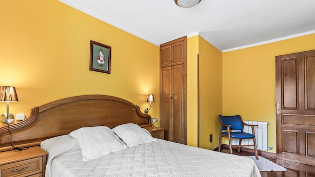 A bedroom with a wooden bed, a nightstand, a chair, and a wardrobe. - Casa Luis with Mountain Views (Llenín)