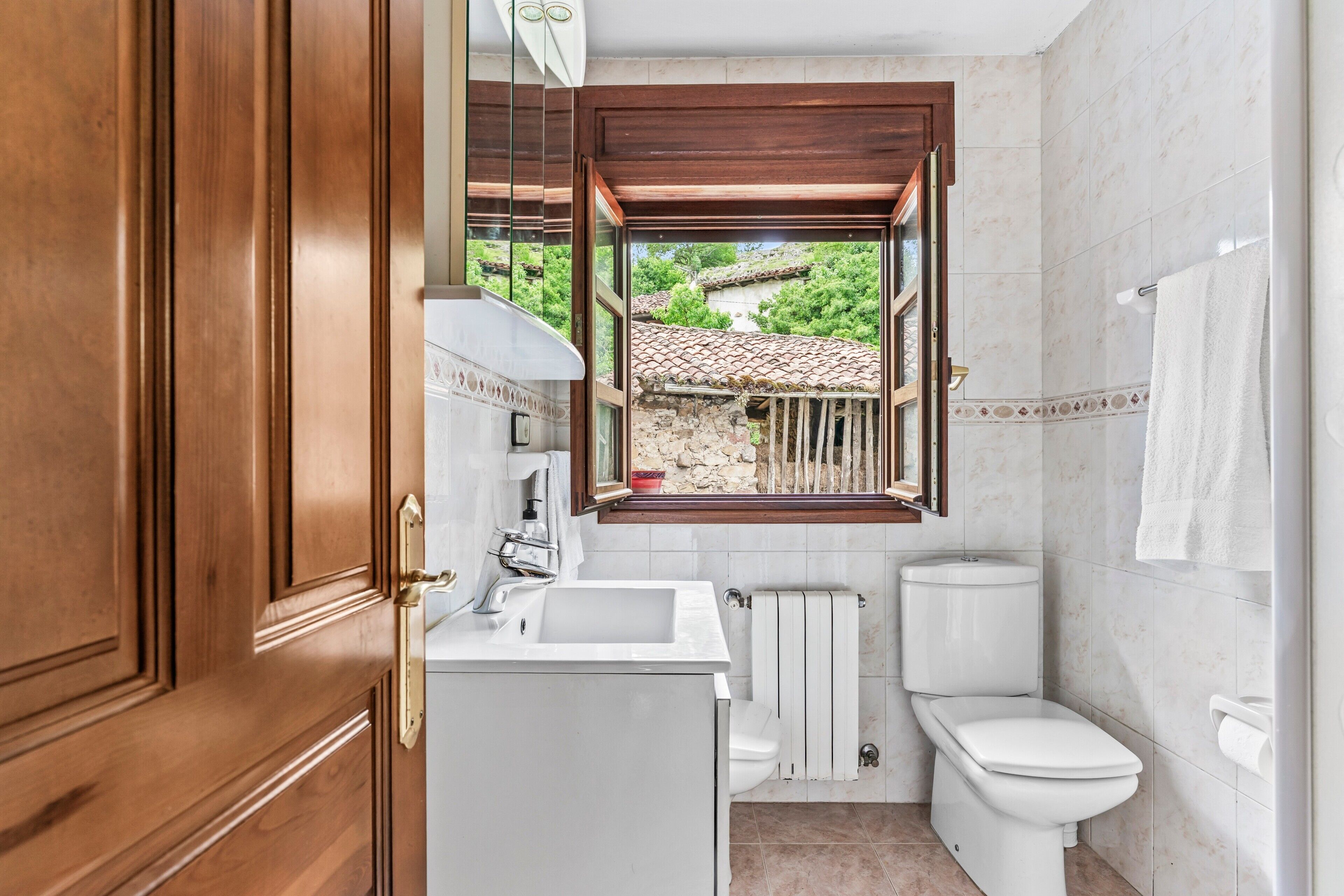 Un bagno con porta in legno, un lavandino, un water, una finestra e un portascopevoli.