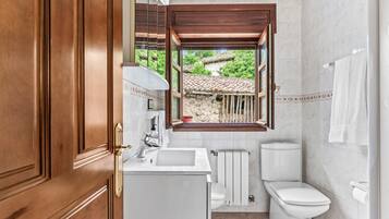 Un bagno con porta in legno, un lavandino, un water, una finestra e un portascopevoli.