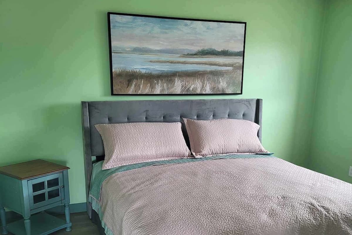 Una cama con cabecera, una mesita de noche y un cuadro en la pared.