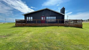 A single-story building with a dark exterior, a red door, and a fenced front yard. - What a View Cheticamp (Chéticamp)
