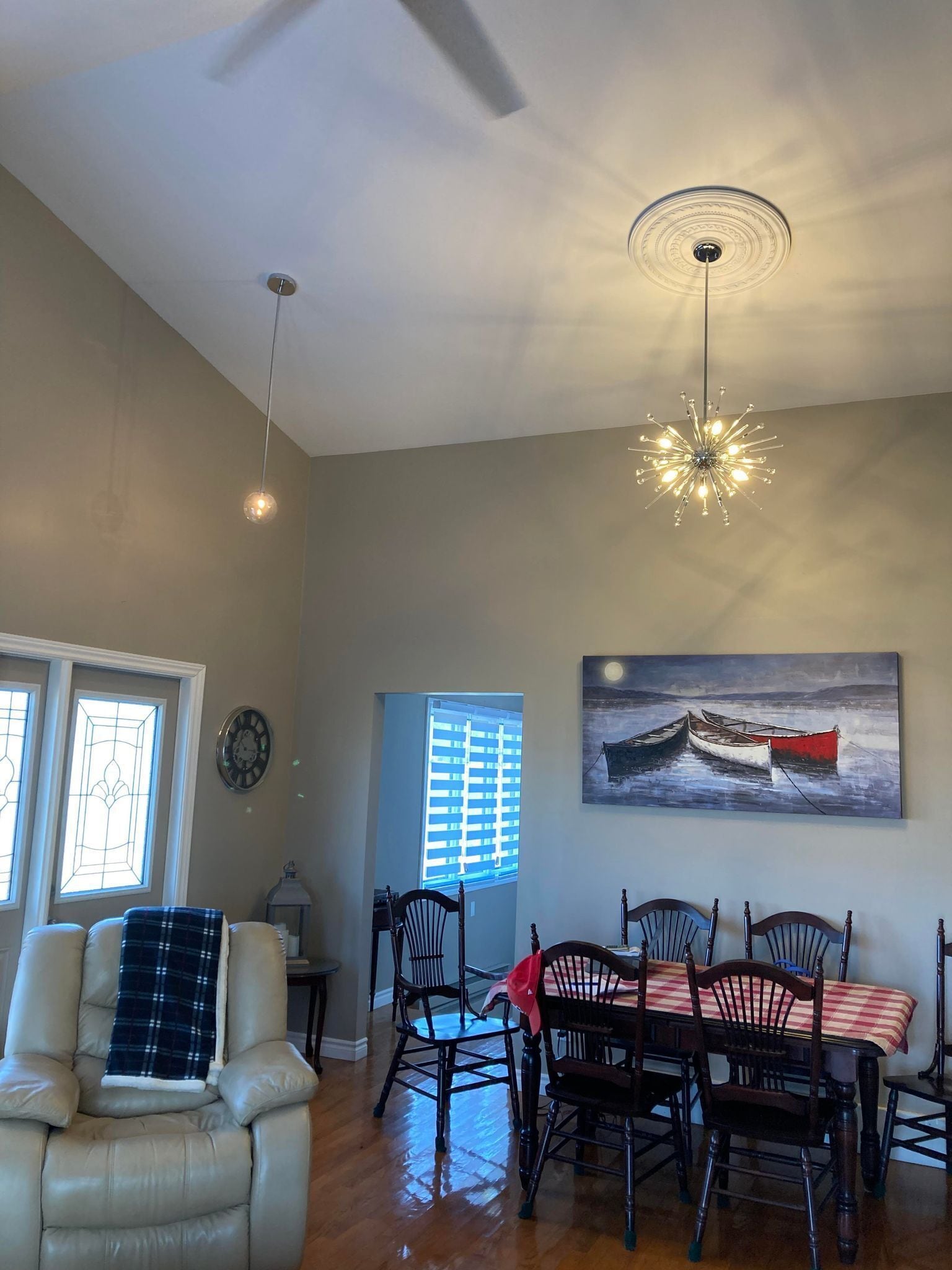 Uma sala de jantar com uma mesa e cadeiras, um ventilador de teto e um quadro na parede.