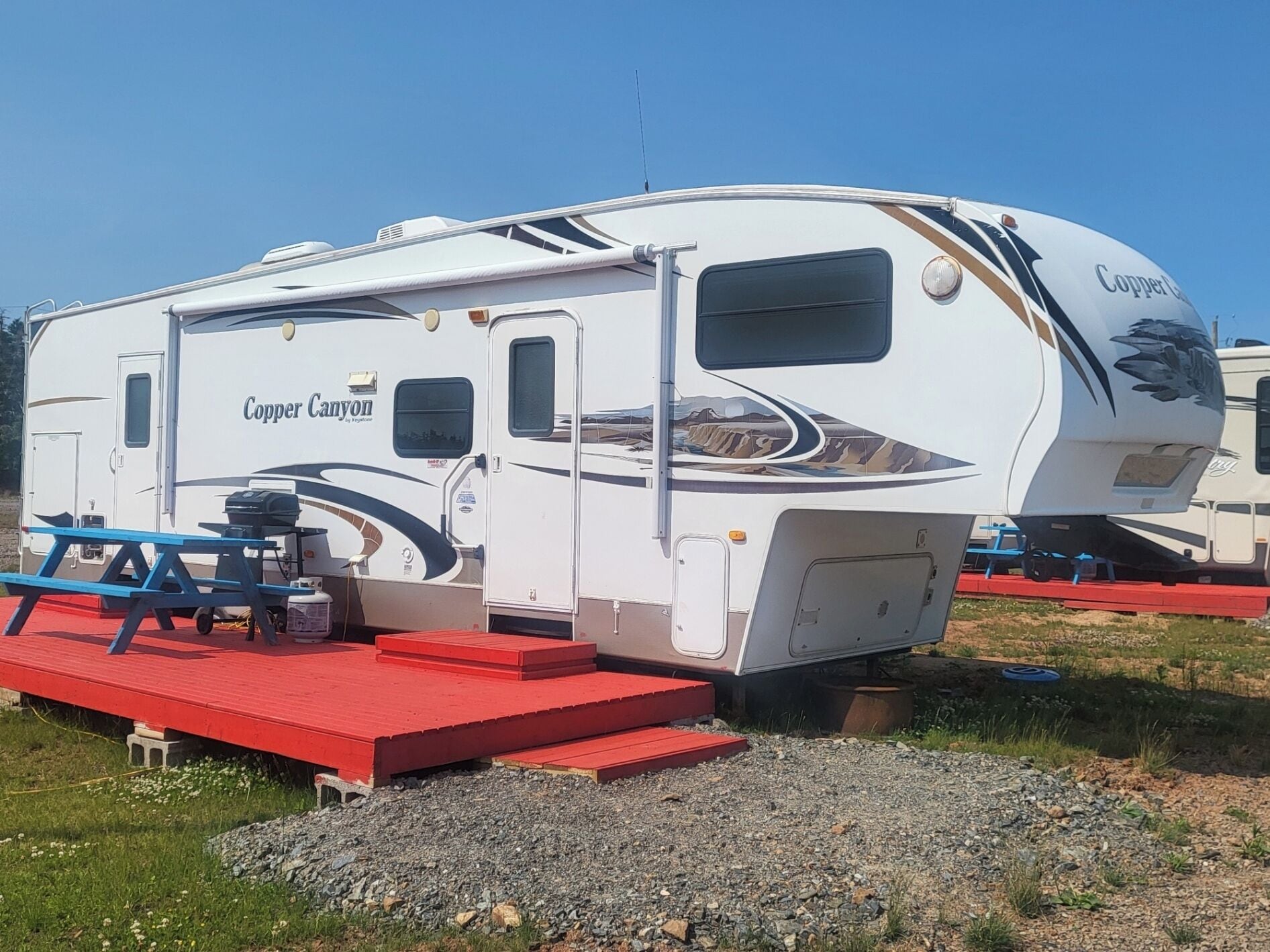 A large RV with a covered front area, a slide-out kitchen, and a small outdoor seating area.