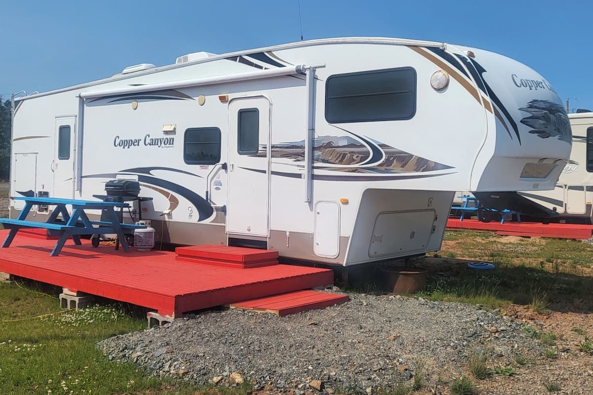Una caravana grande con un porche cubierto, una cocina extensible y una pequeña zona de estar al aire libre.