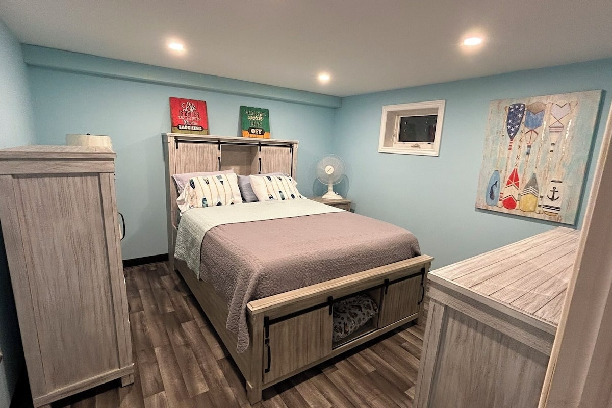 Un dormitorio con una cama, una mesita de noche, un aparador y una pared decorada con motivos náuticos.