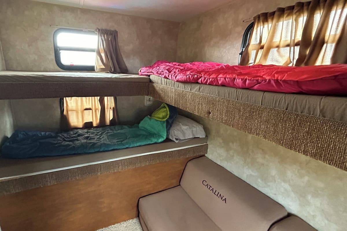 Interior compacto de una autocaravana con literas, una ventana pequeña y un asiento identificado como 'CATALINA'.