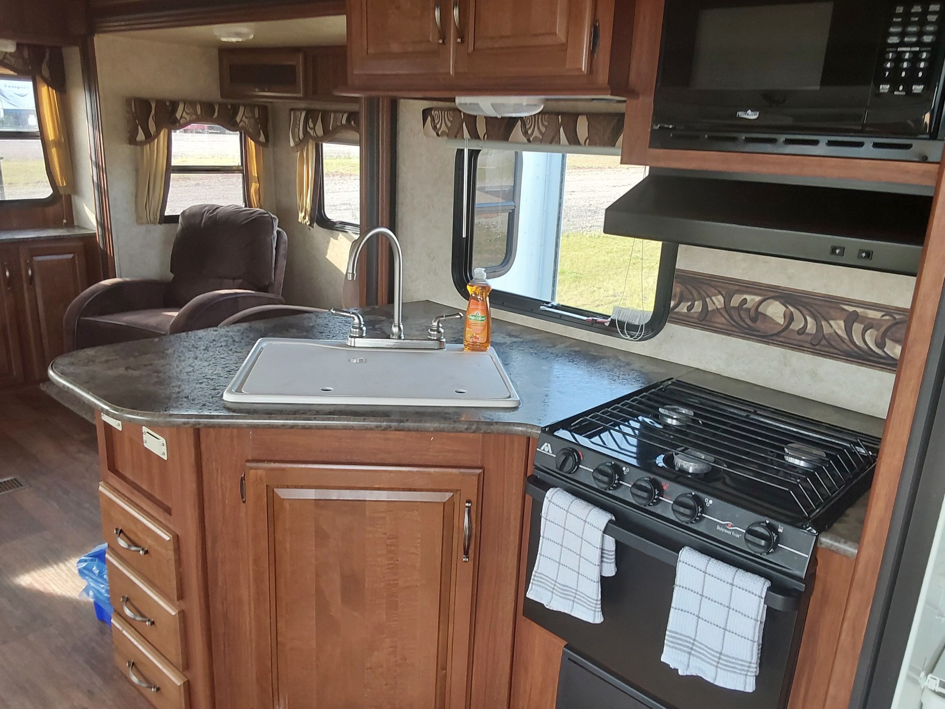 Une cuisine compacte pour camping-car, équipée d’un évier, d’une cuisinière et d’un four à micro-ondes.