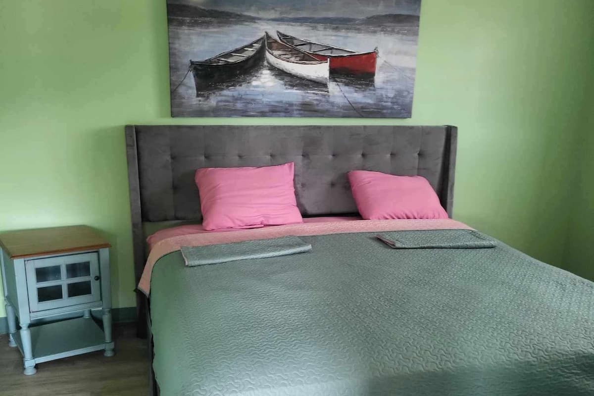 Un dormitorio con cama, mesita de noche, un cuadro y suelo de madera.