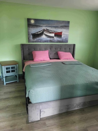 A bedroom with a bed, a nightstand, a painting, and a wooden floor.. What a View Cheticamp