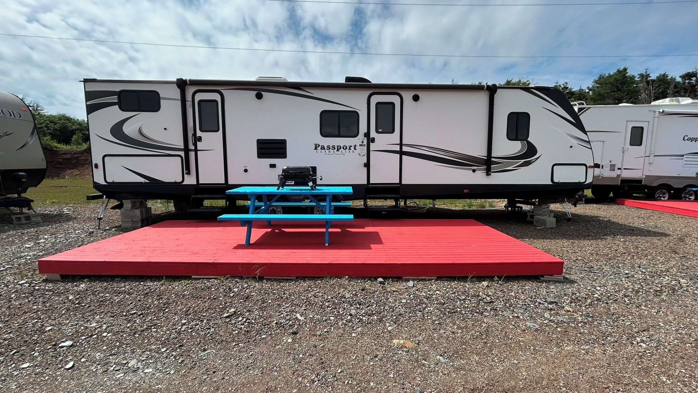 A Passport ULTRALITE Grand Touring RV with a blue picnic table and red platform.