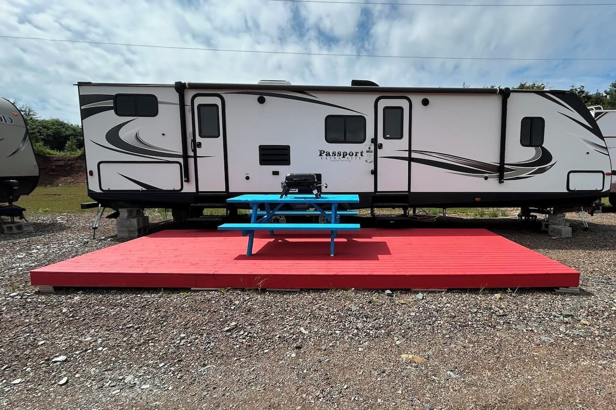 Una caravana Passport ULTRALITE Grand Touring con una mesa de picnic azul y una plataforma roja.