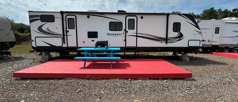 A Passport ULTRALITE Grand Touring RV with a blue picnic table and red platform.