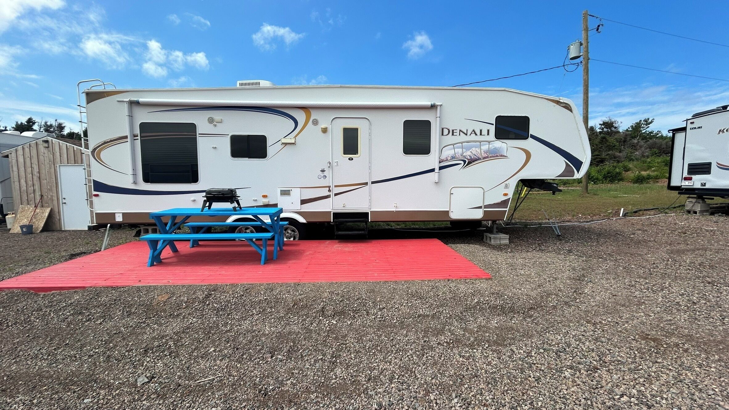 A Denali RV with a red picnic table and a covered picnic area.