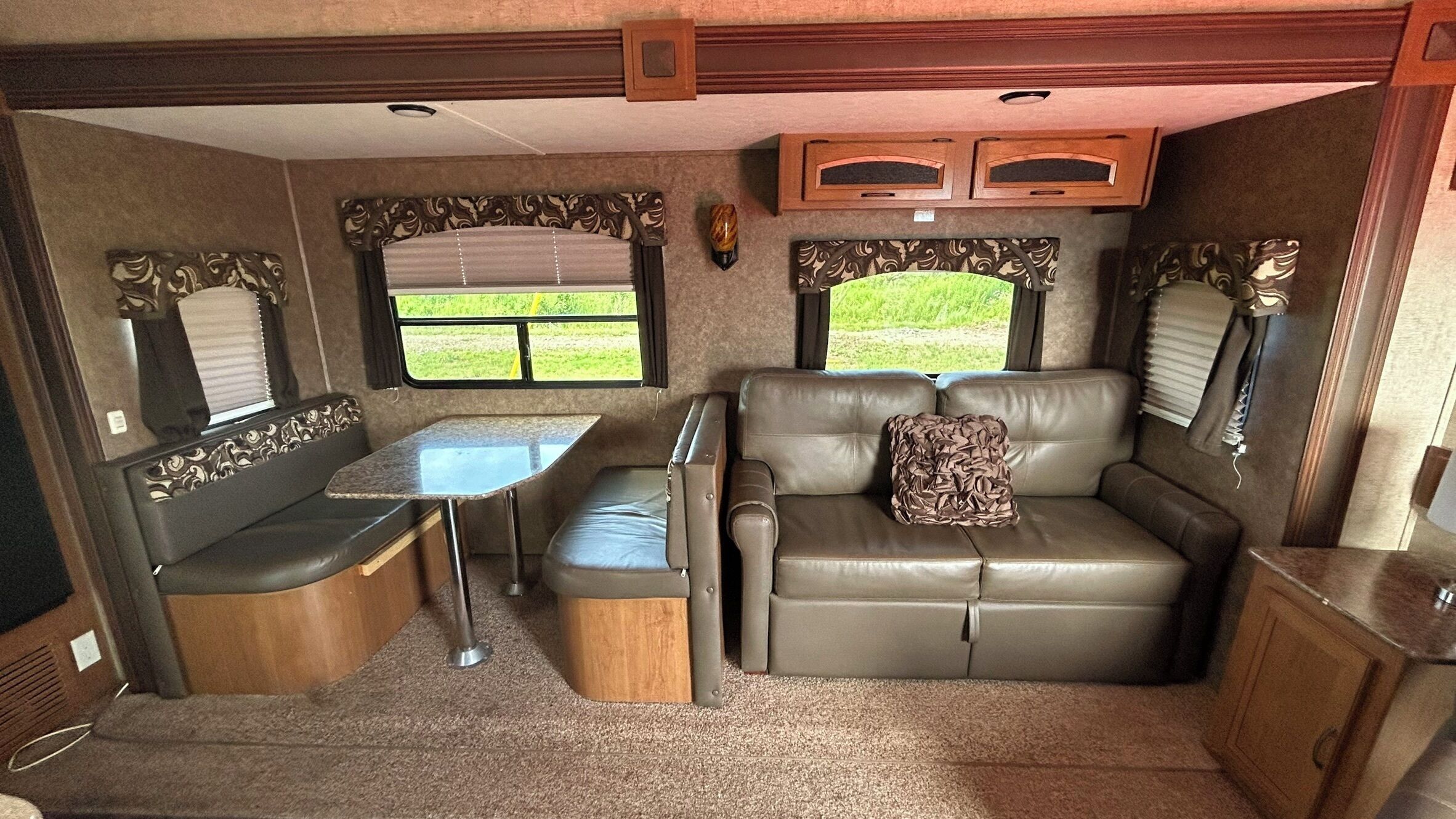 A compact RV interior with a dining table, a sofa, and a small kitchenette.