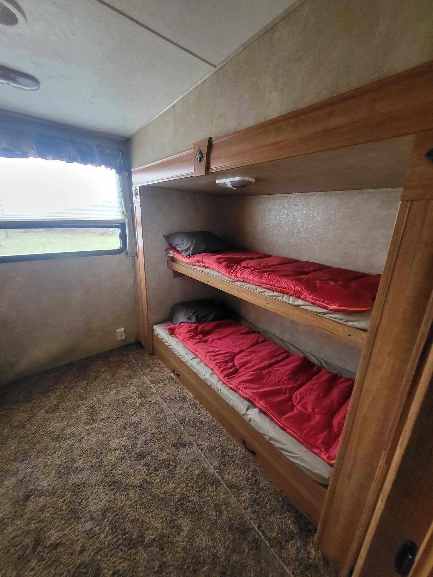 A bunk bed with red bedding, a window, and a ceiling vent.