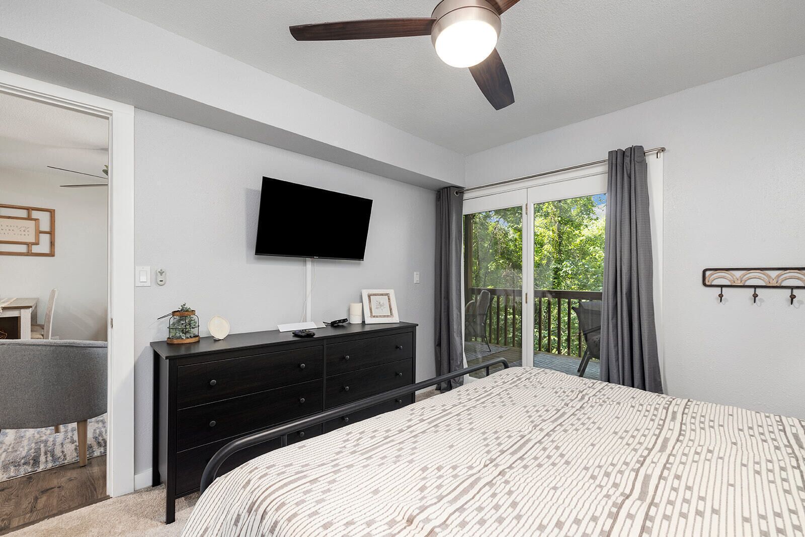 A bedroom with a bed, a dresser, a flat-screen TV, a ceiling fan, and a sliding glass door to a balcony.