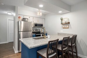 A modern kitchen with granite countertops, stainless steel appliances, and a blue accent wall. - No-Stairs 2BR Branson Retreat w/ Pool, King Bed & SDC (Reeds Spring)