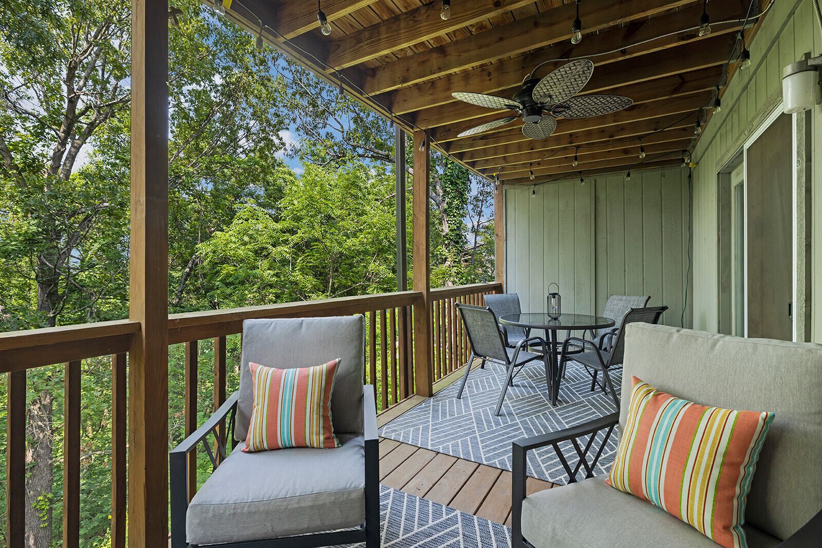 A covered outdoor seating area with wooden railings, a ceiling fan, and a table with chairs.