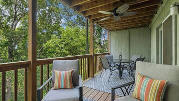 A covered outdoor seating area with wooden railings, a ceiling fan, and a table with chairs.