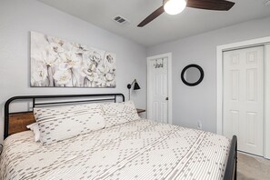 A bedroom with a bed, a ceiling fan, a wall-mounted mirror, and a door. - No-Stairs 2BR Branson Retreat w/ Pool, King Bed & SDC (Reeds Spring)