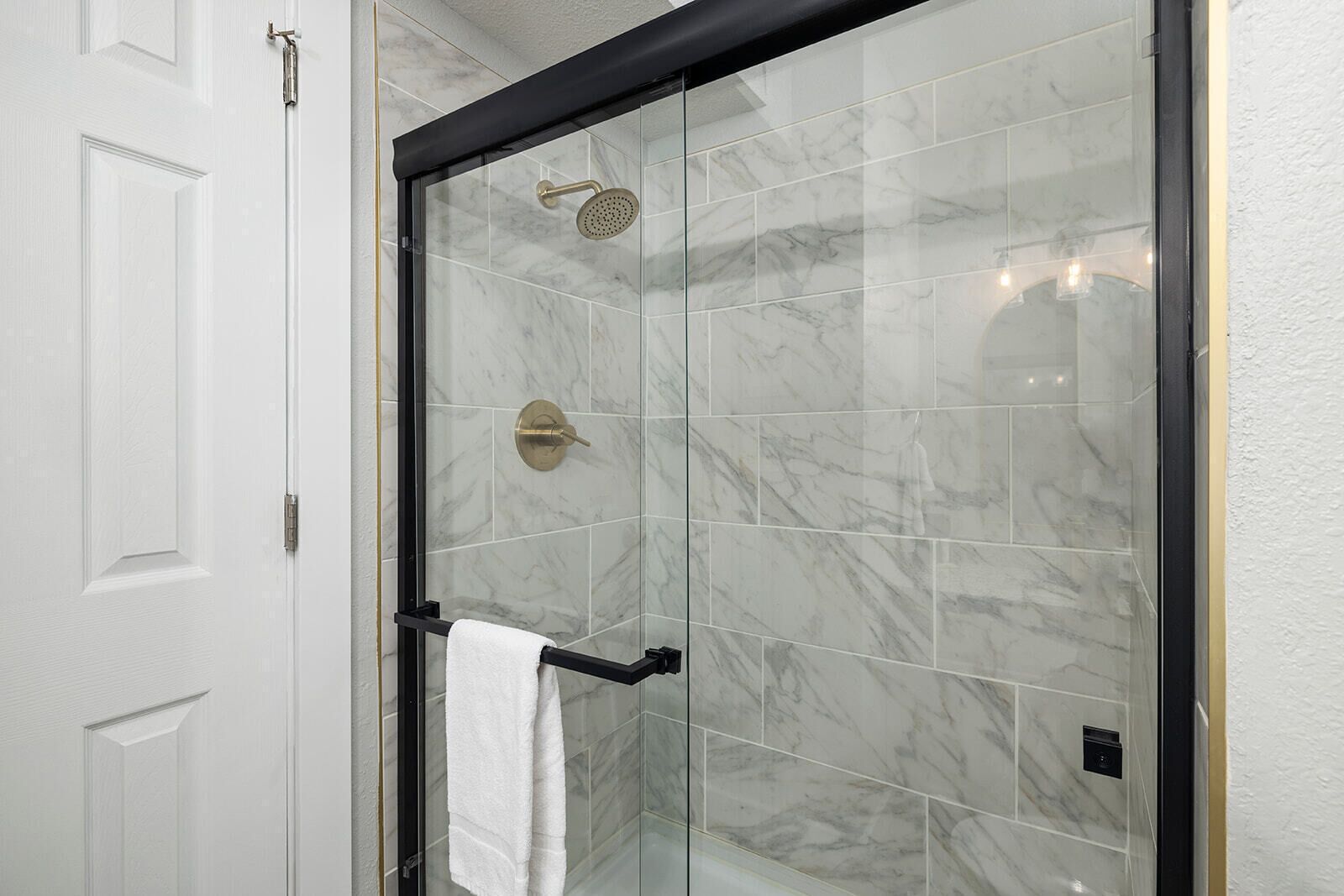 Une douche en verre avec une pomme de douche dorée et un porte-serviettes.