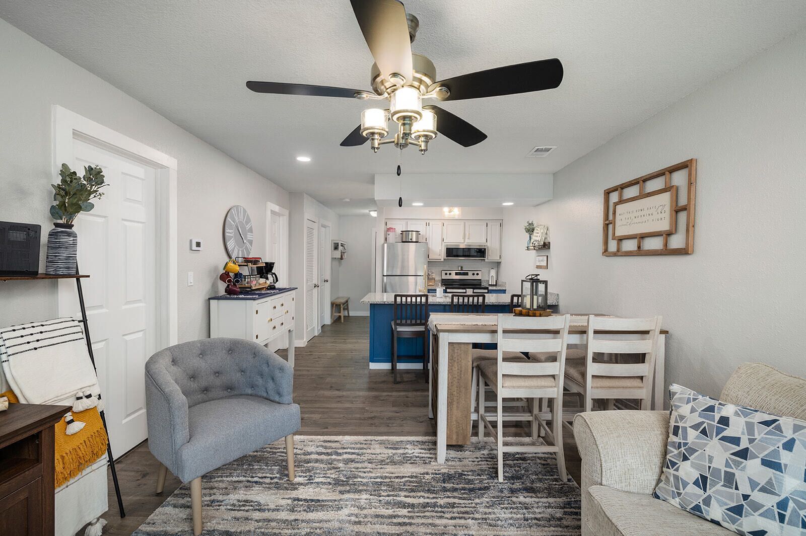 A modern kitchen with white cabinets, a blue island, and a dining area with a white table and chairs.