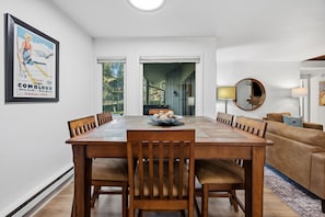 A dining area with a wooden table and chairs, a bowl of cookies, and a poster on the wall. - Modern 3BR Keystone Condo · Sleeps 6 · Walk to Lake, Minutes to Golf (Keystone)