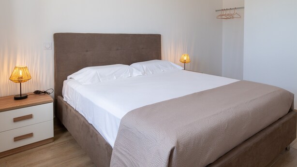 A neatly made bed with a headboard, bedside tables with lamps, and a wall-mounted coat rack. - Apartment 'La Dolce Vita 6' with Sea View, Wi-Fi and Air Conditioning (Borgo)