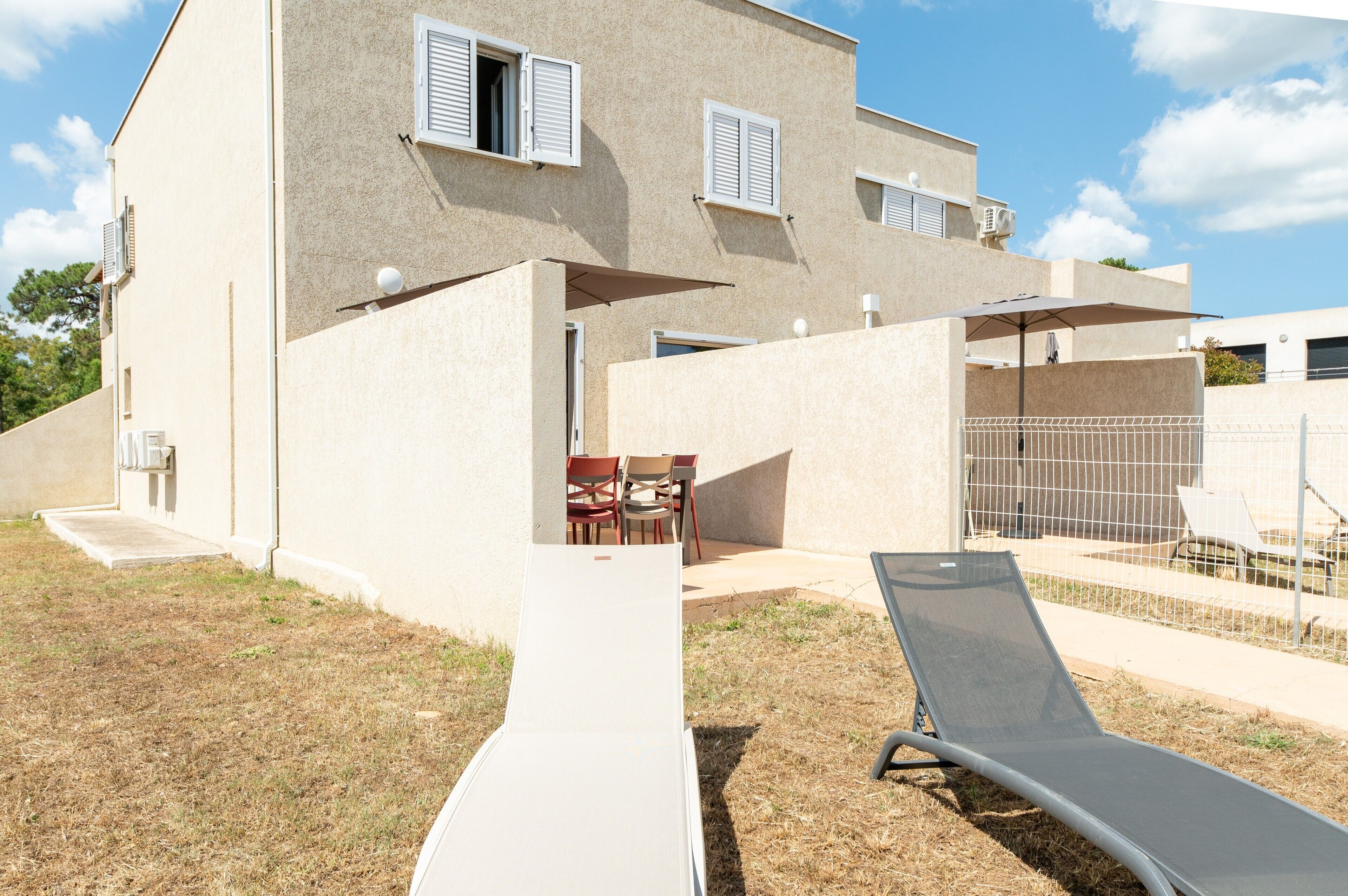 Ein zweistöckiges Gebäude mit Terrasse, Sitzgelegenheiten im Freien und einem Pool.