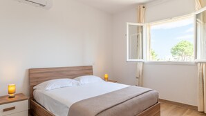 A bedroom with a wooden bed, bedside tables with lamps, a window with curtains, and a view of trees. - Apartment 'Residence La Dolce Vita' with Sea View, Wi-Fi and Air Conditioning (Borgo)