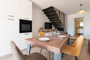 A modern kitchen with white cabinets, a built-in oven, and a dining area with a wooden table and chairs.