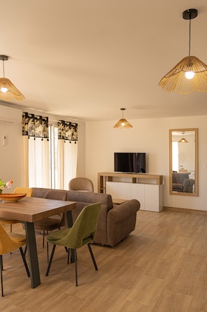 Uma sala de estar moderna com uma mesa de jantar de madeira, duas cadeiras, um sofá e uma TV em um armário branco.