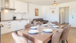 Eine moderne Küche mit weißen Schränken, einem Esstisch für sechs Personen und einem Sofa im Wohnbereich.