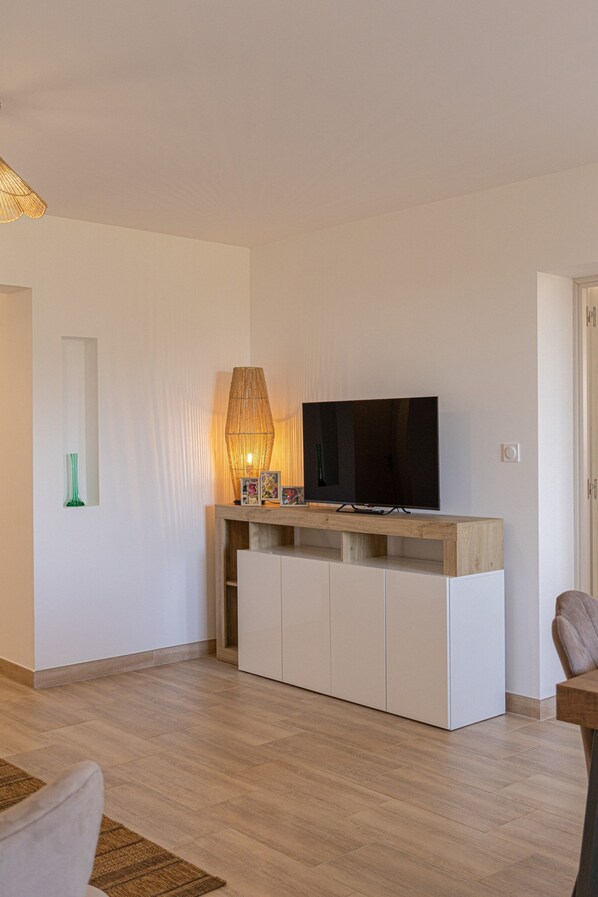 Ein modernes Wohnzimmer mit einem Flachbildfernseher auf einer Holzkonsole, einer Lampe und einer grünen Vase an der Wand.