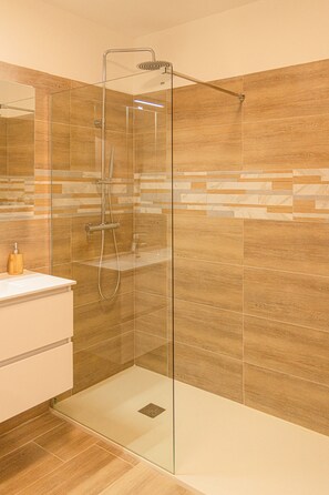 Une salle de bain moderne avec une douche à parois de verre, un meuble-lavabo en bois et un mur recouvert de carreaux.