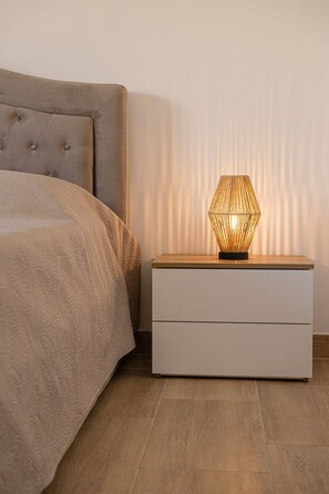 Un lit avec une tête de lit capitonnée, une table de chevet avec une lampe et un plancher en bois.