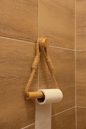 Ein Toilettenpapierhalter mit einer daran befestigten Kordel, an einer Wand mit Holzstruktur.