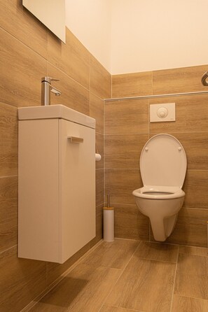 Une salle de bain équipée de toilettes, d’un meuble et d’une poignée de chasse d’eau fixée au mur.