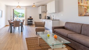 Eine moderne Küche mit weißen Schränken, ein Essbereich mit einem Glastisch und ein braunes Sofa.