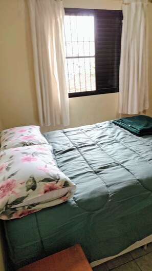 Una habitación con cama, ventana con cortinas y vistas al exterior.