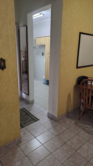 Un pasillo con piso de baldosas, una silla de madera, un perchero y un espejo en la pared.