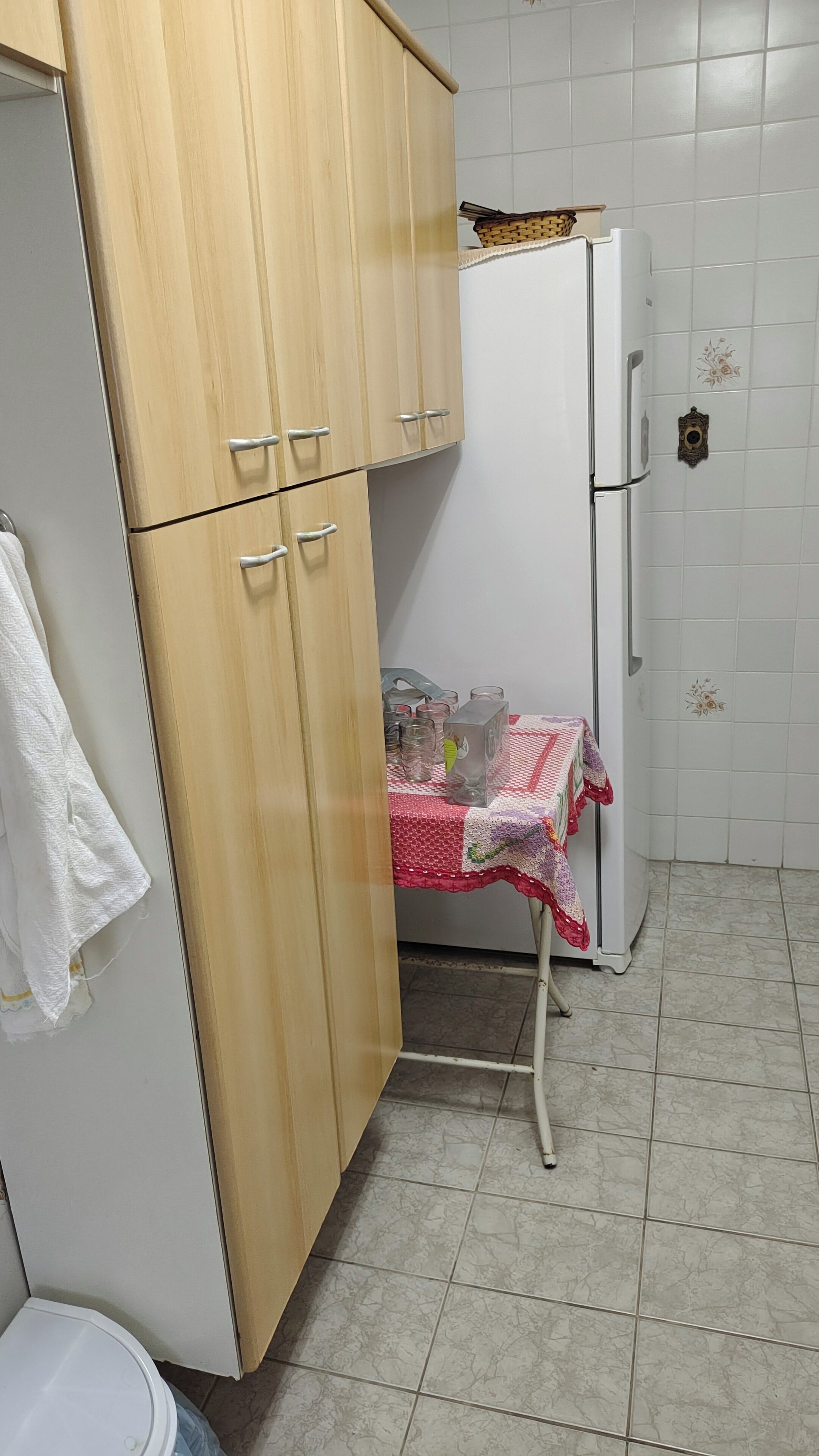Keittiössä on puukuvioiset kaapit, valkoinen jääkaappi, laatoitettu seinäosa työtason yläpuolella ja pöytä, jonka päällä on punavalkoinen pöytäliina.