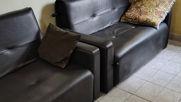 A black leather sofa with a patterned throw pillow, a brown cushion, and a framed picture on the wall.