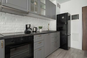 A kitchen with grey cabinets, a black refrigerator, a coffee maker, and a stainless steel oven.