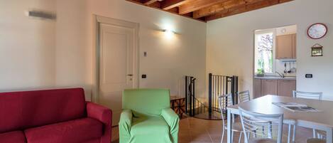 Un salon avec un canapé rouge, un fauteuil vert et une table à manger avec des chaises.