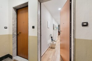 Un corridoio con una porta in legno, un vaso bianco con un ombrello e un citofono a parete.