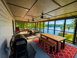 A room with a large window overlooking a lake, a wooden table, a bench, and a sofa. - Lakefront Paradise in Double Springs, AL 6BR Cabin with Private Dock (Double Springs)